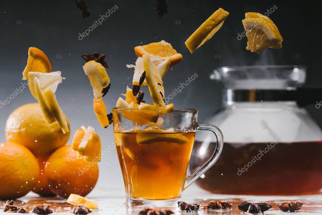 Glass cup of hot steaming tea with falling citrus pieces