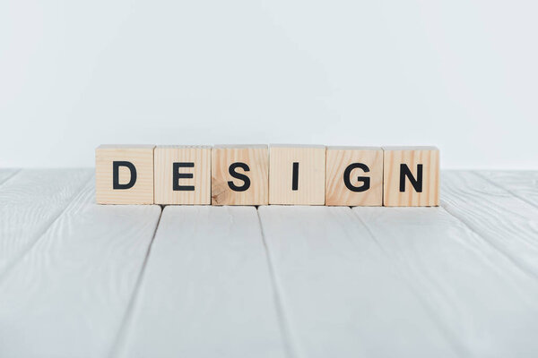 close up view of design word made of wooden cubes on white wooden tabletop 