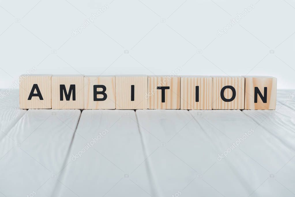 close up view of ambition word made of wooden cubes on white wooden tabletop 