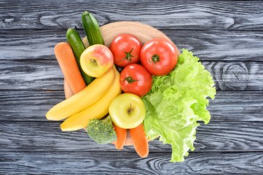 top view of fresh ripe fruits and vegetables on plate on wooden table clipart