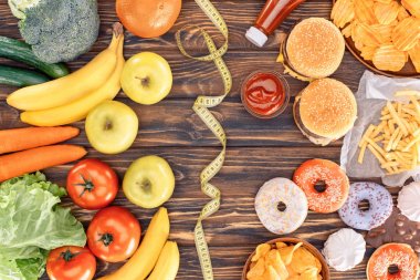 top view of assorted junk food, fresh fruits with vegetables and measuring tape on wooden table    clipart
