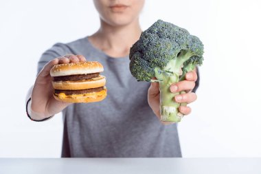 close-up view of woman holding fresh ripe broccoli and hamburger  clipart