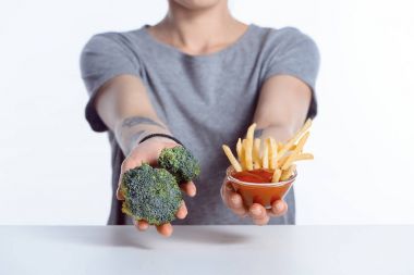 cropped shot of girl holding fresh broccoli and ketchup with french fries clipart