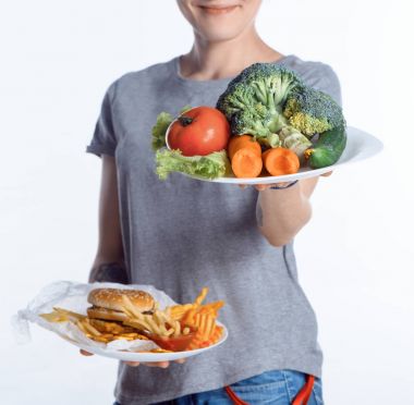 cropped shot of woman holding plates with vegetables and junk food clipart