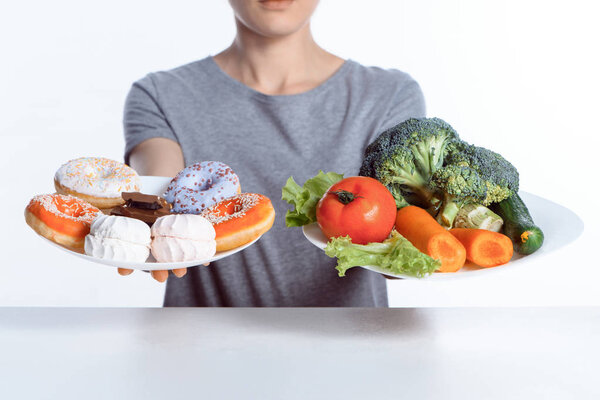 cropped shot of woman holding plates with sweets and vegetables
