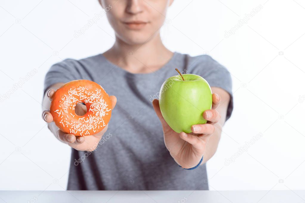 cropped shot of girl holding fresh apple and donut