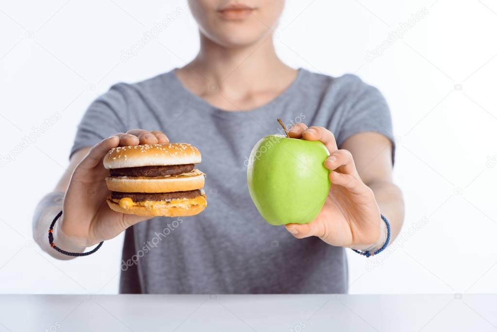 close-up view of woman holding fresh ripe apple and hamburger 