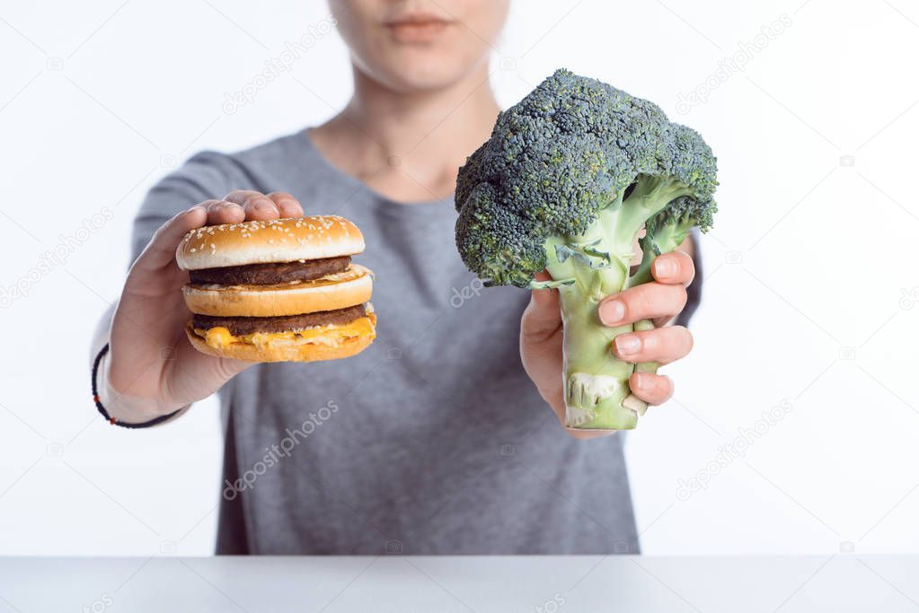 close-up view of woman holding fresh ripe broccoli and hamburger 
