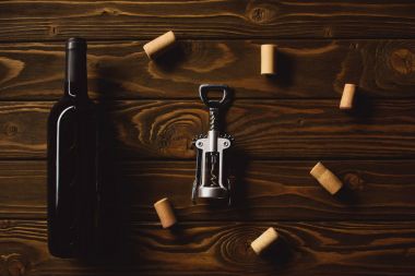 top view of bottle of luxury red wine with corkscrew surrounded with corks on wooden table clipart