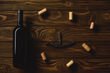 top view of bottle of red wine with corkscrew surrounded with corks on wooden table clipart