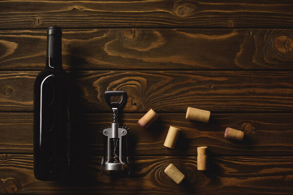 top view of bottle of luxury red wine with corks and corkscrew on wooden table