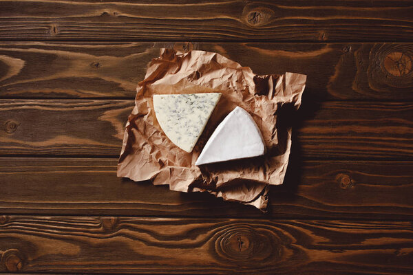 top view of slices of cheese on crumpled paper on wooden table