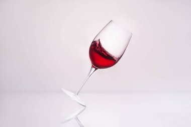 inclined wineglass with splashing red wine on reflective surface and on white clipart