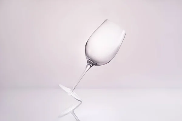 empty inclined wineglass on reflective surface and on white