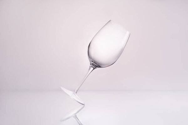 empty inclined wineglass on reflective surface and on white