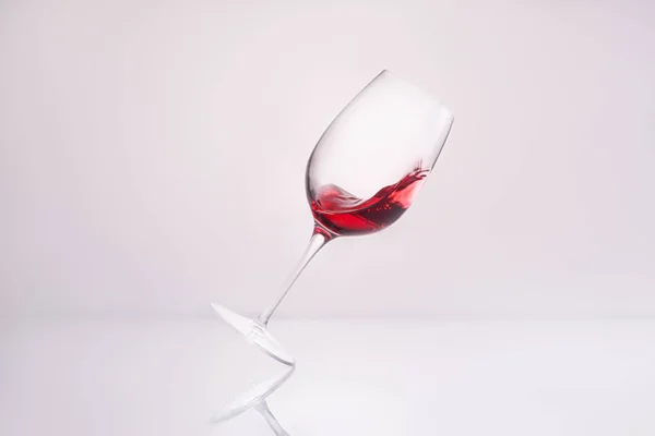 Vidro Inclinado Com Vinho Tinto Espirrando Superfície Reflexiva Branco — Fotografia de Stock