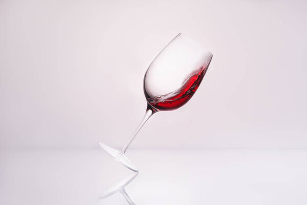 inclined wineglass with red wine on reflective surface and on white