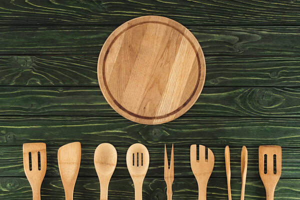 top view of round cutting board and kitchen utensils placed in row on wooden table 