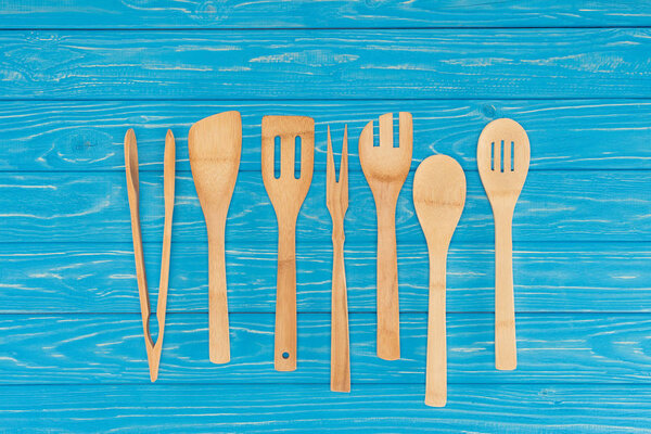 top view of wooden kitchen utensils placed in row on blue table 
