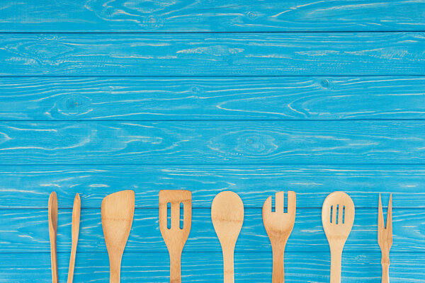 top view of wooden kitchen utensils placed in row on blue table 