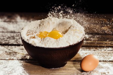 yolks falling into bowl with flour on wooden table with one egg near clipart