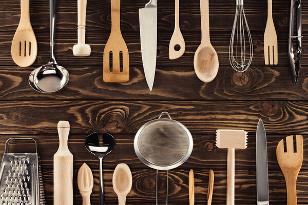 top view of different kitchen utensils placed in two rows on wooden table
