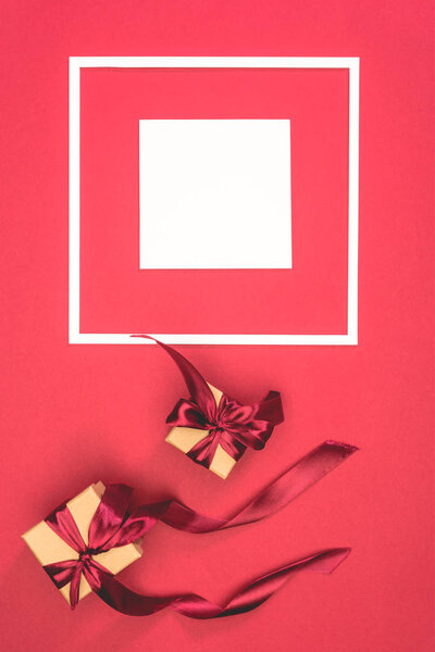 top view of gift boxes with ribbons and frame with cube on red surface
