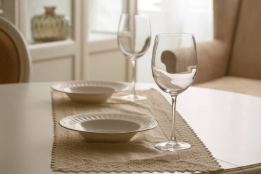 Wineglasses and white plates on table in dining room clipart