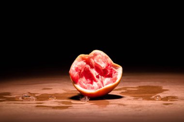 squeezed grapefruit on wooden table in dark room clipart