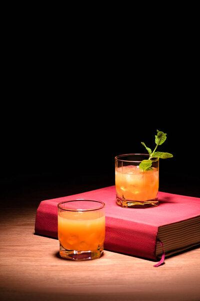 orange alcohol cocktails with mint on pink book on table