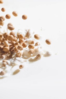Soybeans falling in milk with drops on white background clipart