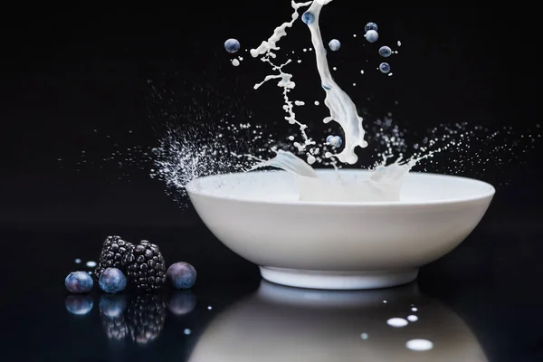 在黑色背景下用牛奶在白色碗里飞溅的新鲜浆果 — 免费的图库照片