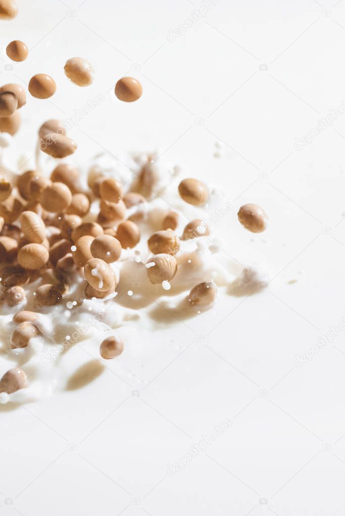 Soybeans falling in milk with drops on white background