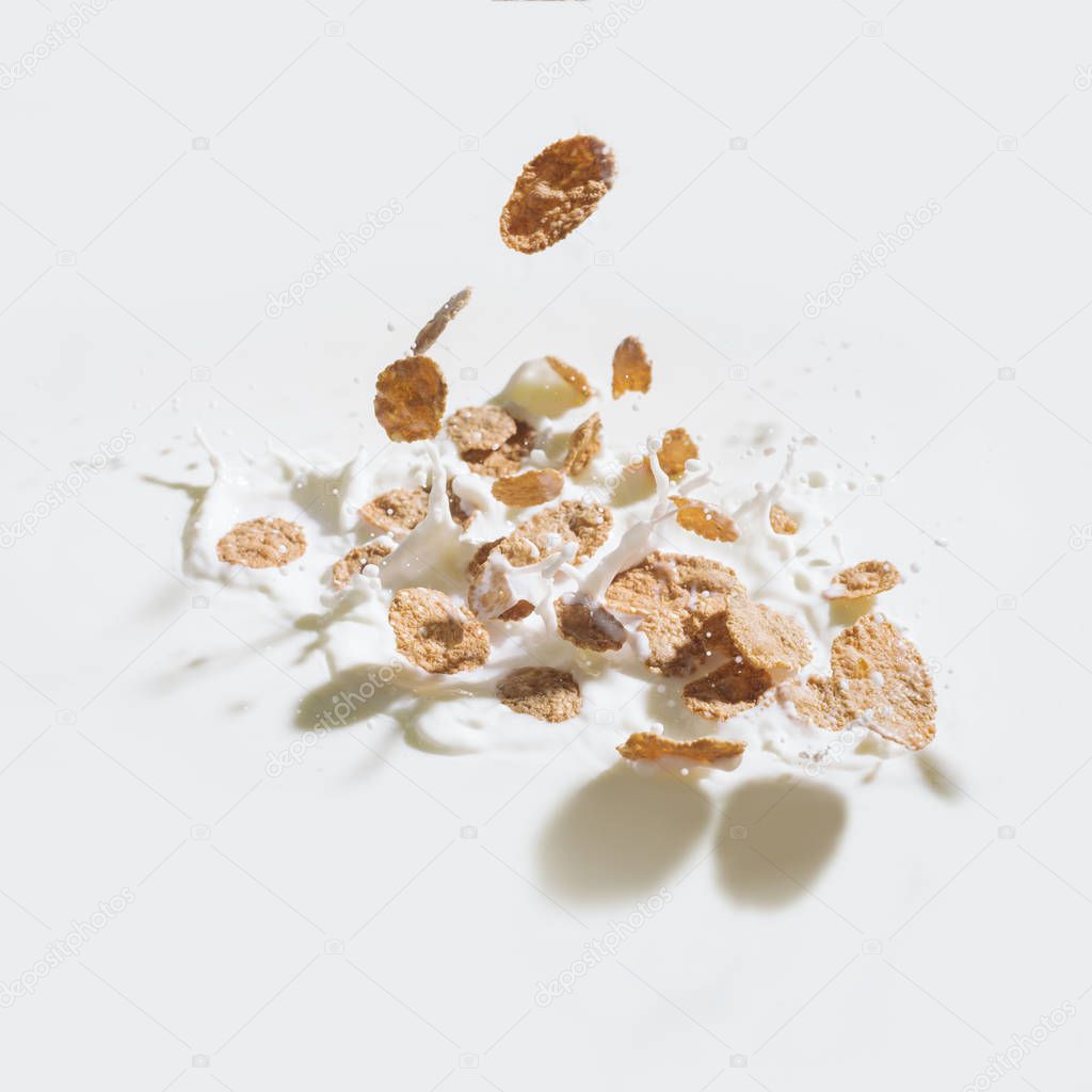 Cornflakes falling in milk with drops on white background