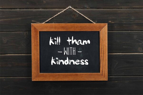 blackboard with kill tham with kindness inscription hanging on wooden wall 