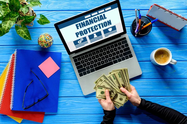 İş kişi ile kırtasiye, mavi ahşap masa üstünde laptop tarafından dolar sayma finansal koruma yazı
