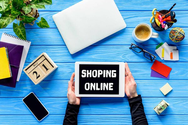 руки держат планшет на синем деревянном столе с деньгами и канцелярскими принадлежностями, онлайн шоппинг
