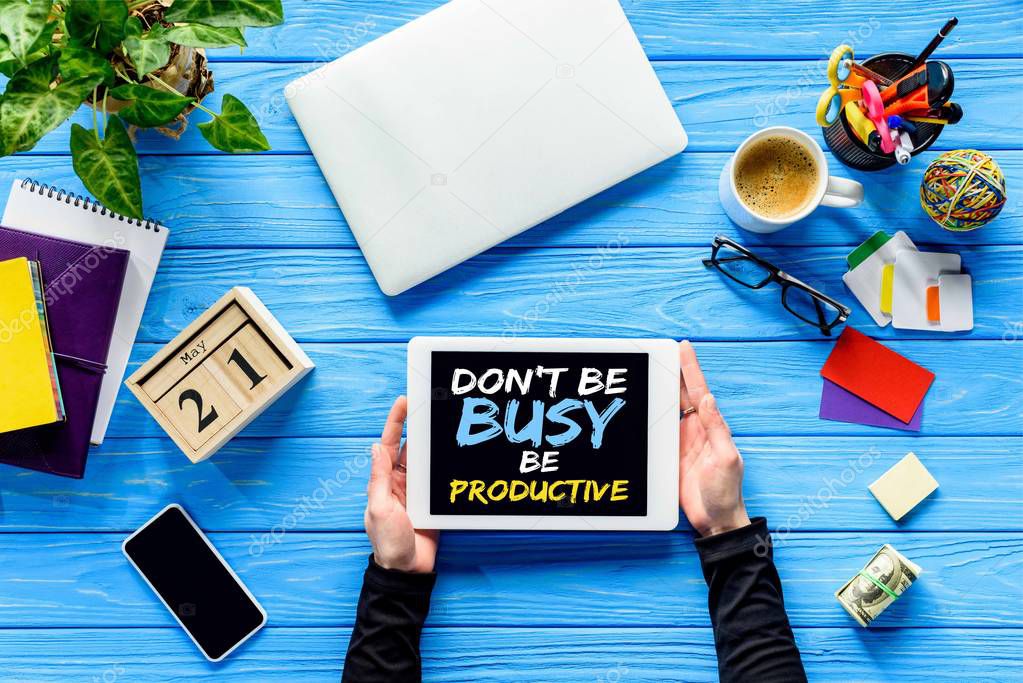 hands holding tablet on blue wooden table with money and stationery, Dont be busy be productive lettering 