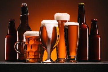 close up view of bottles and mugs of beer on orange background clipart