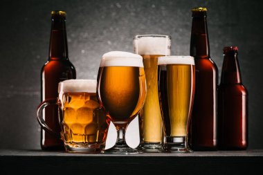 close up view of bottles and mugs of beer on grey background clipart