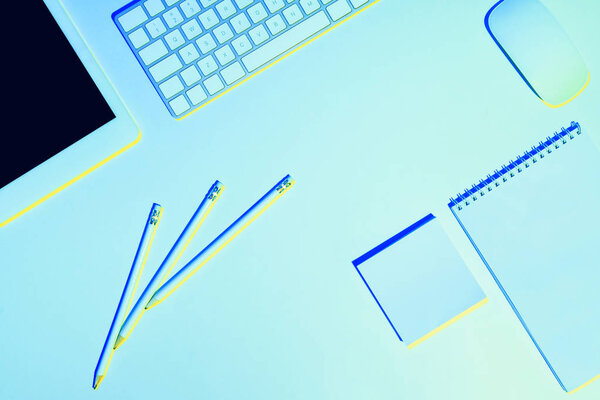 blue toned picture of pencils, digital tablet, computer keyboard and mouse, textbook and sticky note 