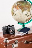retro film camera with flight tickets and globe on vintage suitcase isolated on white