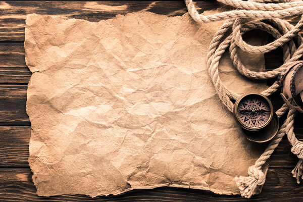 top view of navigation compass and rope on blank crumpled paper