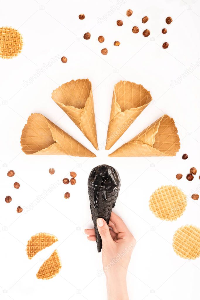 cropped image of woman holding black ice cream in cone under empty ice cream cones isolated on white
