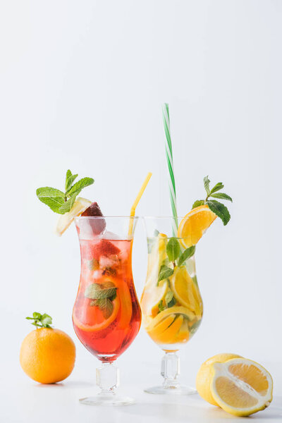 close up view of summer fresh cocktails with strawberry, lemon and oranges, mint and straws isolated on white
