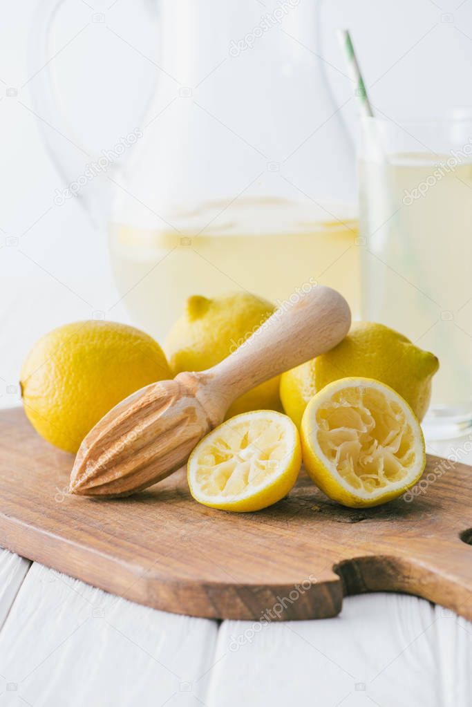 selective focus of lemons and wooden squeezer on cutting board for making fresh lemonade on white wooden tabletop