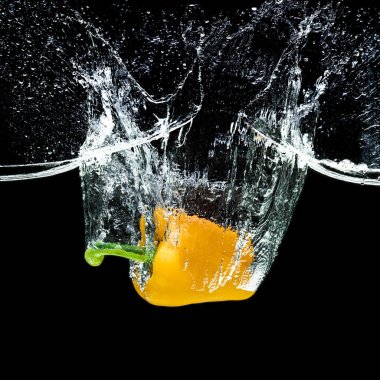 close up view of motion of yellow bell pepper falling into water isolated on black clipart