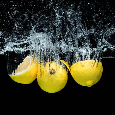 close up view of fresh lemons in water with splashes isolated on black clipart