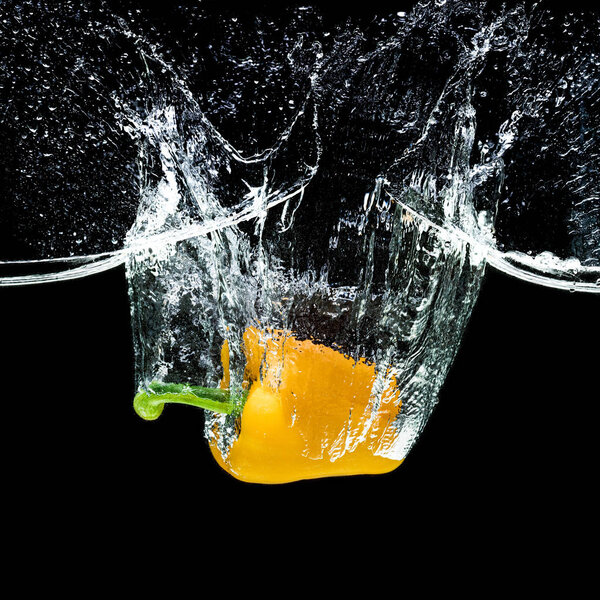 close up view of motion of yellow bell pepper falling into water isolated on black