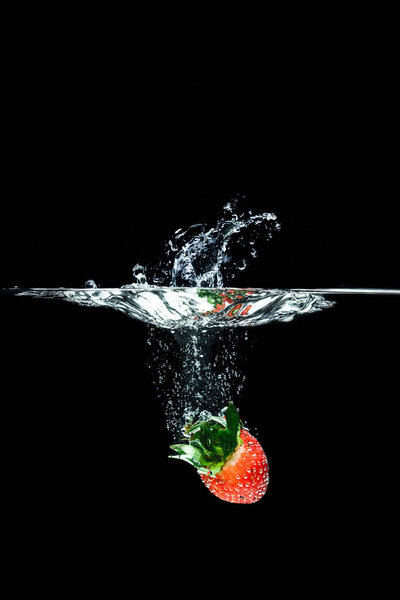 закрытый вид на падающую в воду клубнику, изолированную от черного
